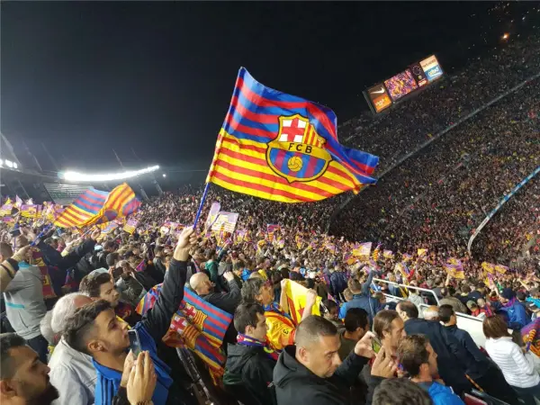 Tłum kibiców na stadionie unosi flagi z herbem FC Barcelona. Flaga Katalonii powiewa dumnie nad głowami fanów.