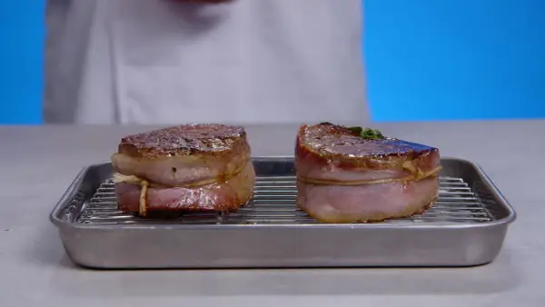 Deux filets mignons enveloppés de lard, prêts pour la cuisson, sur une grille dans un plat.