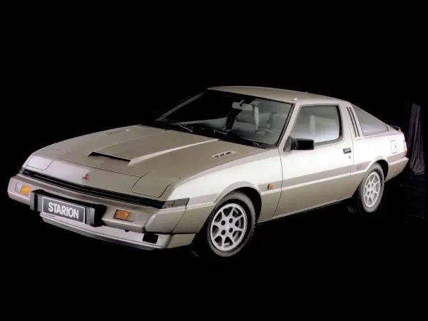 Klasyczny Mitsubishi Starion w kolorze szampańskim, z charakterystycznym wlotem powietrza na masce i sportowym nadwoziem coupe.