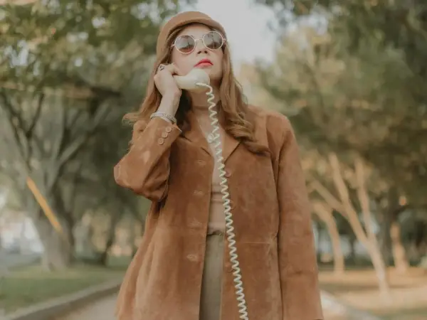 Kobieta w brązowej zamszowej kurtce damskiej rozmawia przez telefon w stylu retro.