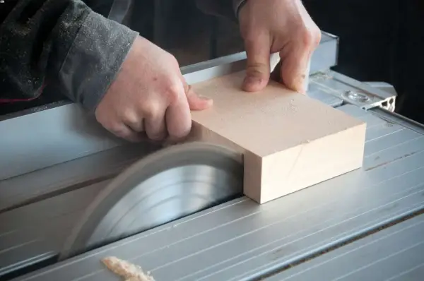 Mani esperte guidano un pezzo di legno su una sega circolare per tagliare legno a mano con precisione.