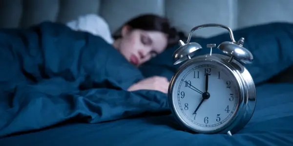 Frau schläft tief, während ein Wecker die Zeit anzeigt. Wie viel Schlaf braucht man mit 40? Die Antwort liegt im erholsamen Schlaf.