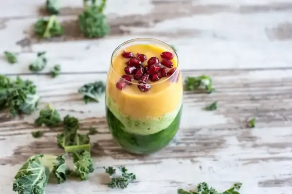 Warstwowy koktajl z jarmużu, mango i granatu, ozdobiony pestkami granatu.