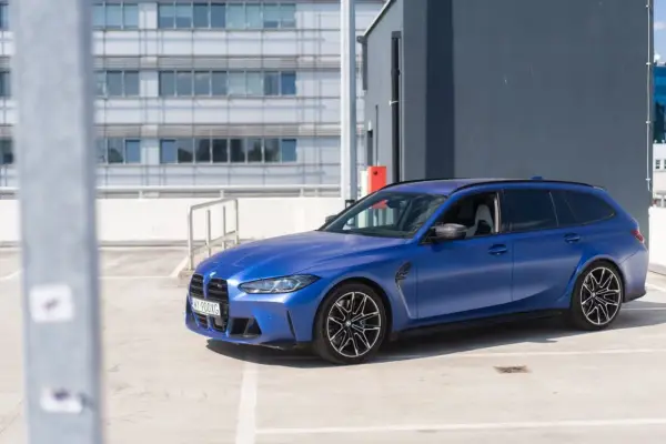 Niebieskie BMW G81 na parkingu, z nowoczesnym budynkiem w tle.