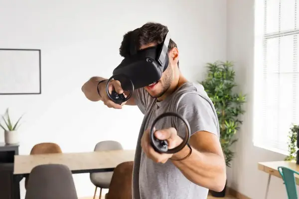 Hombre con casco de RV, inmerso en uno de los mejores juegos VR, con mandos en mano.