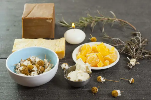 Bienenwachs, Kräuter und Seife für DIY-Kosmetik auf dunklem Holztisch.
