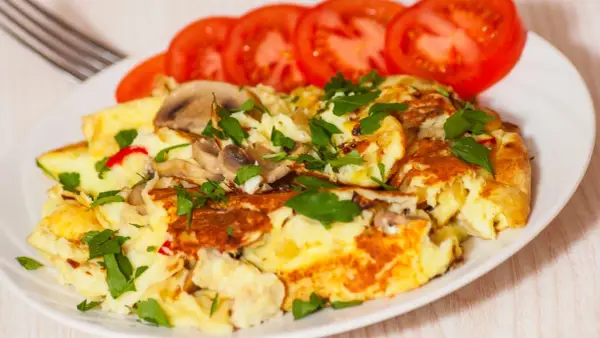 Pyszny omlet jajeczny z pieczarkami i natką pietruszki, podany z plastrami pomidora. Idealny na śniadanie.