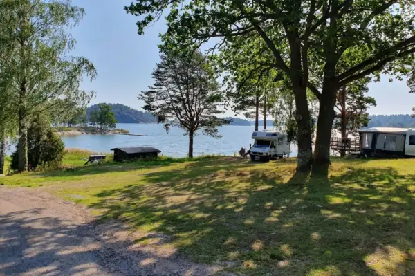 Solig dag vid vattnet på Kalvholmens camping. Husbilar och husvagnar står uppställda på gräsmattan nära sjön.