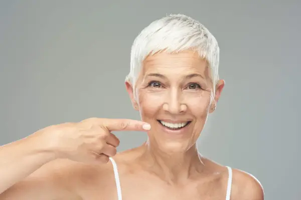 Donna sorridente indica il suo sorriso, un esempio di come rinforzare i denti a cinquant'anni con un sorriso smagliante.