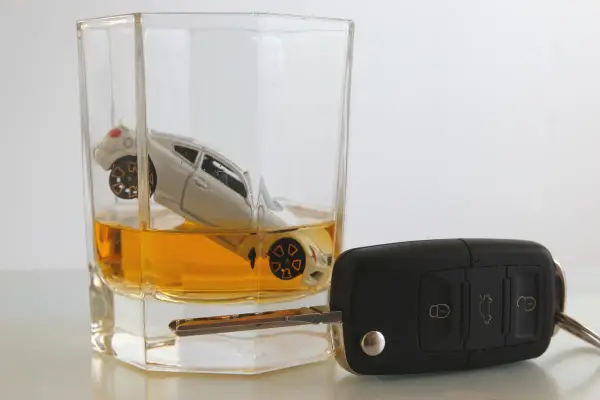 Miniaturowy samochód w szklance z bursztynowym płynem, obok kluczyki. Zastanawiasz się, ile ml ma shot wódki, ale pamiętaj: jazda po alkoholu to ryzyko.