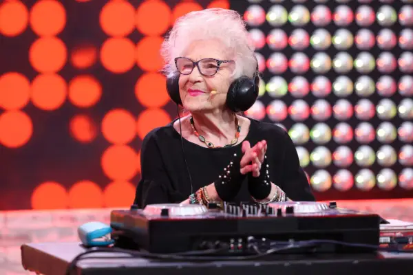 DJ Wika w słuchawkach, z uśmiechem na twarzy, miksuje muzykę. W tle czerwone i białe światła.