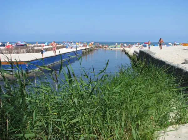 Słoneczny dzień nad kanałem w Karwi. Ludzie odpoczywają na plaży, a woda przyciąga do kąpieli. To jedna z wielu atrakcji w okolicy.