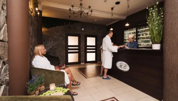 Recepcja w hotelu dla dorosłych. Kobieta w szlafroku siedzi, mężczyzna rozmawia z pracownikiem.