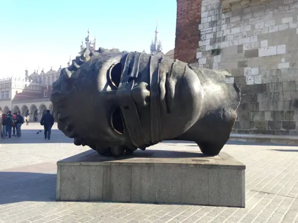 Gigantyczna, metalowa głowa, dzieło polskiego rzeźbiarza, leży na cokole na krakowskim Rynku.