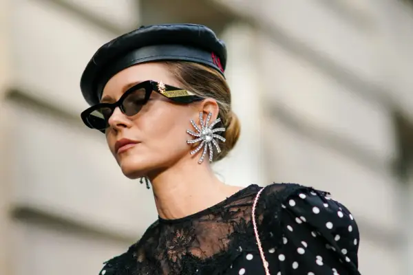 Kobieta w czarnym beretce i okularach przeciwsłonecznych, z dużą, błyszczącą kolczykiem. Czy grochy są modne? Ta stylizacja sugeruje, że tak!