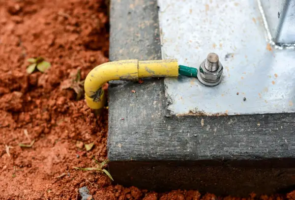 Connexion de la prise de terre maison à une structure métallique, assurant la sécurité électrique. Le câble jaune est relié à une cosse verte, fixée par un boulon.