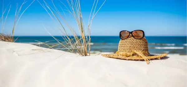 Słomkowy kapelusz z okularami przeciwsłonecznymi na piaszczystej plaży, idealny na wyjazd gdzie nad morze.