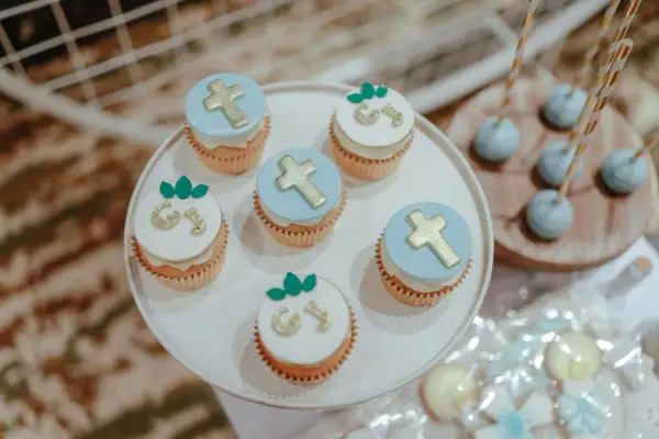 Jolis cupcakes décorés de croix dorées et de lettres pour un buffet dessert baptême. Des cake pops bleus sont aussi présents.