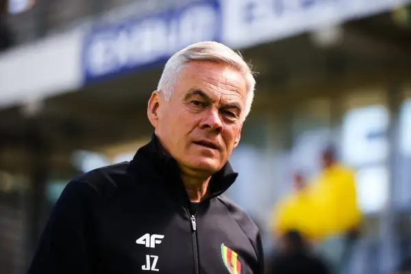 Jacek Zieliński, doświadczony trener, w czarnej kurtce z logo 4F i inicjałami JZ, na tle stadionu.
