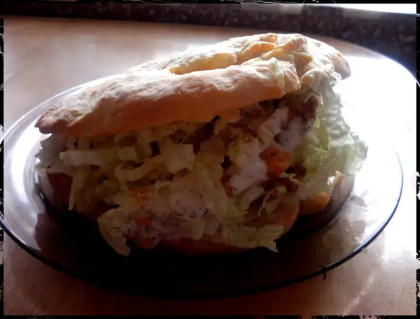 Pyszny kebab w bułce z chrupiącą sałatą i kremowym sosem, gotowy do zjedzenia.
