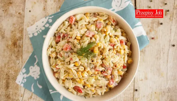 Pyszna sałatka z makaronem orzo, szynką, kukurydzą i ogórkiem, udekorowana koperkiem. Idealna na letnie dni.