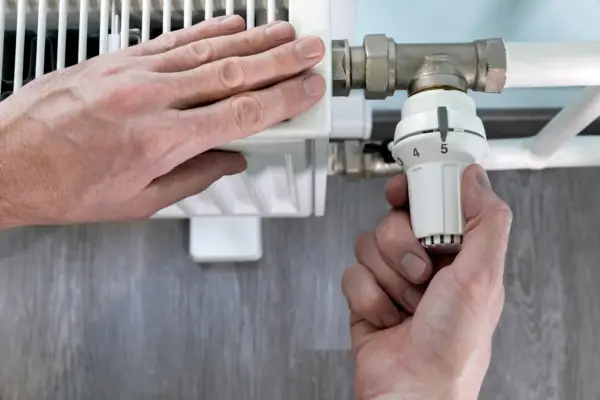 Mano ajusta el termostato de un radiador. El radiador solo calienta la mitad derecha, indicando un posible problema.
