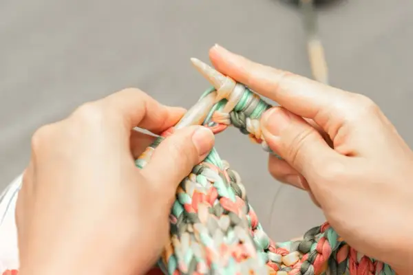 Dłonie dziergają kolorową włóczkę na drutach. Czy na Vinted można sprzedawać handmade? Tak, to świetne miejsce na rękodzieło!