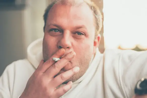 Hombre con cigarrillo en la mano, con el pelo rubio y ojos azules. Fumar hace que se te caiga el pelo.