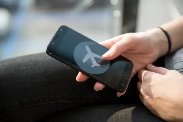 Dłoń trzyma smartfon z ikoną samolotu. Zastanawiasz się, czy w trybie samolotowym działa budzik?