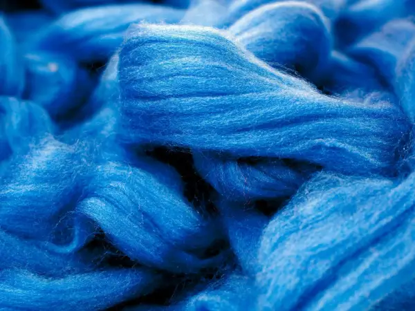 Leuchtend blaue Fasern, die an Wolle erinnern. Obwohl sie sich wie eine Naturfaser anfühlt, ist Viskose eine künstlich hergestellte Faser.