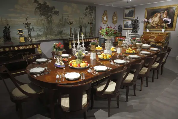 Table dressée dans un style directoire, avec fruits, fleurs et vaisselle raffinée. Le décor mural évoque un paysage champêtre.