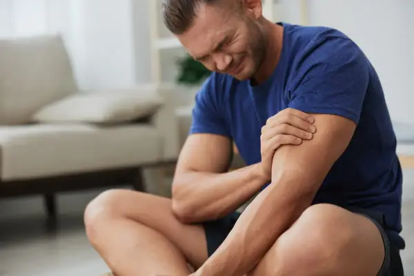 Hombre con expresión de dolor, sujetando su brazo. Sufre de dolores musculares tras un esfuerzo.