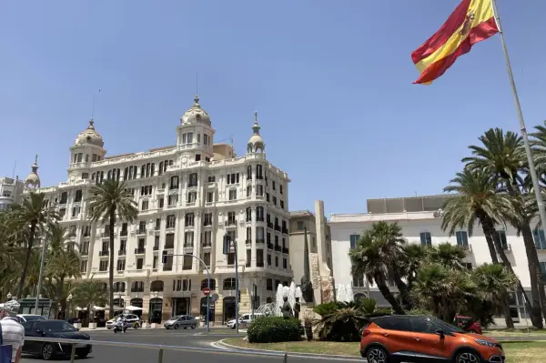 Alicante, pogoda marzec: słoneczny dzień, palmy i hiszpańska flaga nad białym budynkiem.