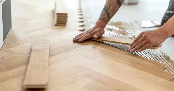 Pose de lames de parquet en bois, créant un motif en chevrons. L'isolation du sol est assurée par la colle appliquée.