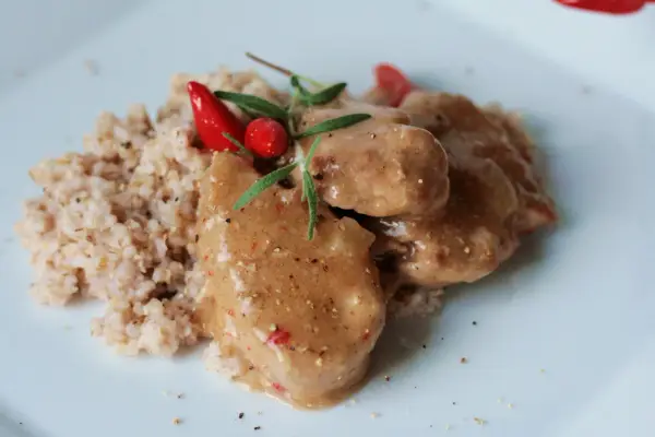 Polędwiczki wieprzowe w sosie własnym, danie Ani gotuje, podane z kaszą i ozdobione papryczką chili i rozmarynem.