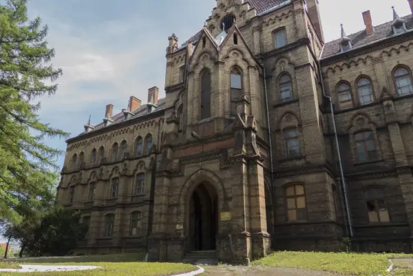 Mokrzeszów pałac, monumentalna budowla z cegły, z charakterystycznymi łukami i wieżyczkami, otoczona zielenią.
