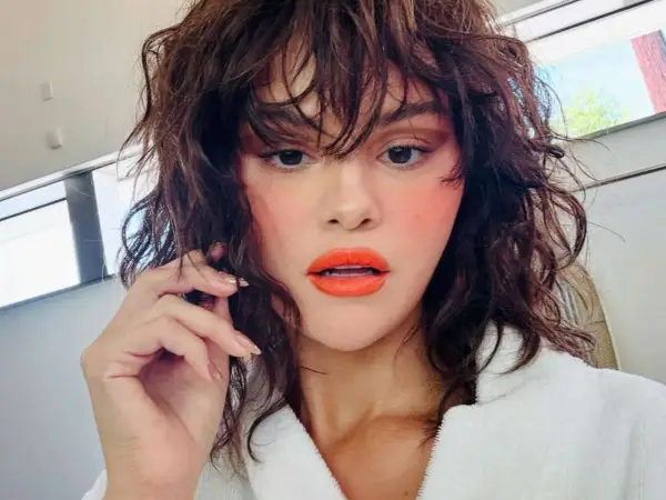Selena Gomez w wolf cut, z pomarańczową szminką i różowymi policzkami. Fryzura pasuje do odważnych stylizacji.