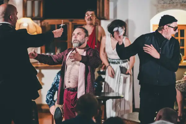 Aktorzy na scenie, w tym mężczyzna z brodą w rozpiętej koszuli, prezentują swój repertuar. Widownia w napięciu obserwuje rozwój wydarzeń.