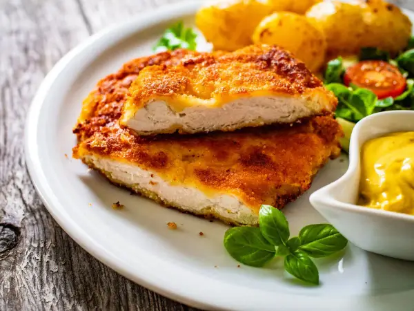 Pyszny kotlet po parysku, chrupiący i złocisty, podany z ziemniaczkami, sałatką i musztardą.
