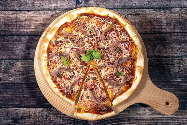 Une pizza savoureuse aux anchois, oignons rouges et câpres, garnie de fromage râpé et de basilic frais, prête à être dégustée.