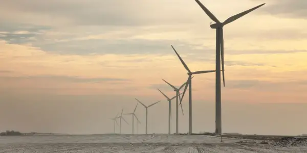 Rząd potężnych farm wiatrowych na tle zachodzącego słońca, tworzący malowniczy krajobraz.