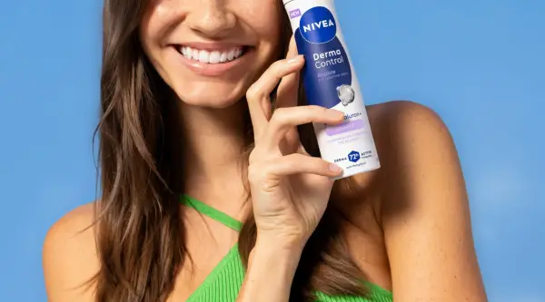 Uśmiechnięta kobieta trzymająca dezodorant Nivea Derma Control na tle niebieskiego tła.