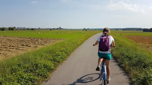 Dziewczynka na rowerze przemierza malowniczą wiślaną trasę rowerową Niepołomice, mijając pola z sianem i zielone łąki.