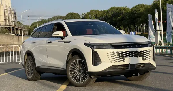 Biały OMODA 9 Super Hybrid z czerwonym wnętrzem na tle przemysłowego krajobrazu.