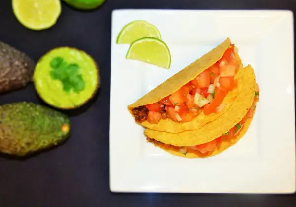 Pyszne meksykańskie tacos przepis na talerzu, z awokado i limonką w tle. Idealne na szybki obiad!