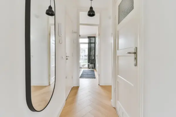 Un ampio specchio nel corridoio riflette le porte bianche e il pavimento in parquet.