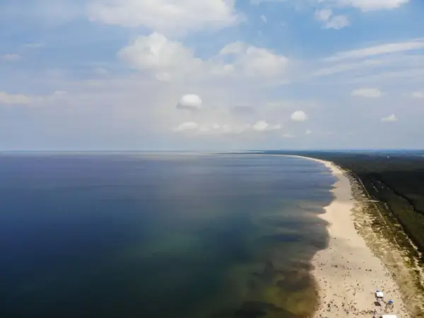 Szeroka, piaszczysta sobieszewo plaża z mnóstwem ludzi wypoczywających nad spokojnym morzem.