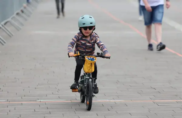 Małe dziecko w kasku i okularach przeciwsłonecznych śmiga na rowerze, wyciągając język. To dziecko na rowerze przepisy, jak prawdziwy mistrz.