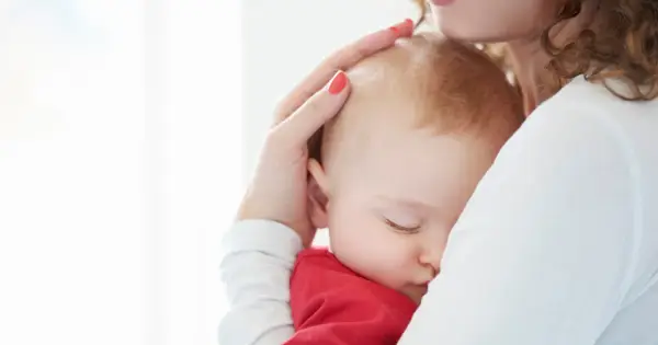 Ciemiączko przednie niemowlęcia delikatnie dotykane przez matkę. Dziecko śpi wtulone w jej ramię.