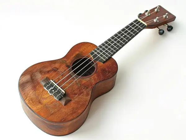 Drewniane ukulele z widocznymi śladami użytkowania. Na gryfie widać progi, a na pudle rezonansowym struny. Idealne do nauki chwytów na ukulele.